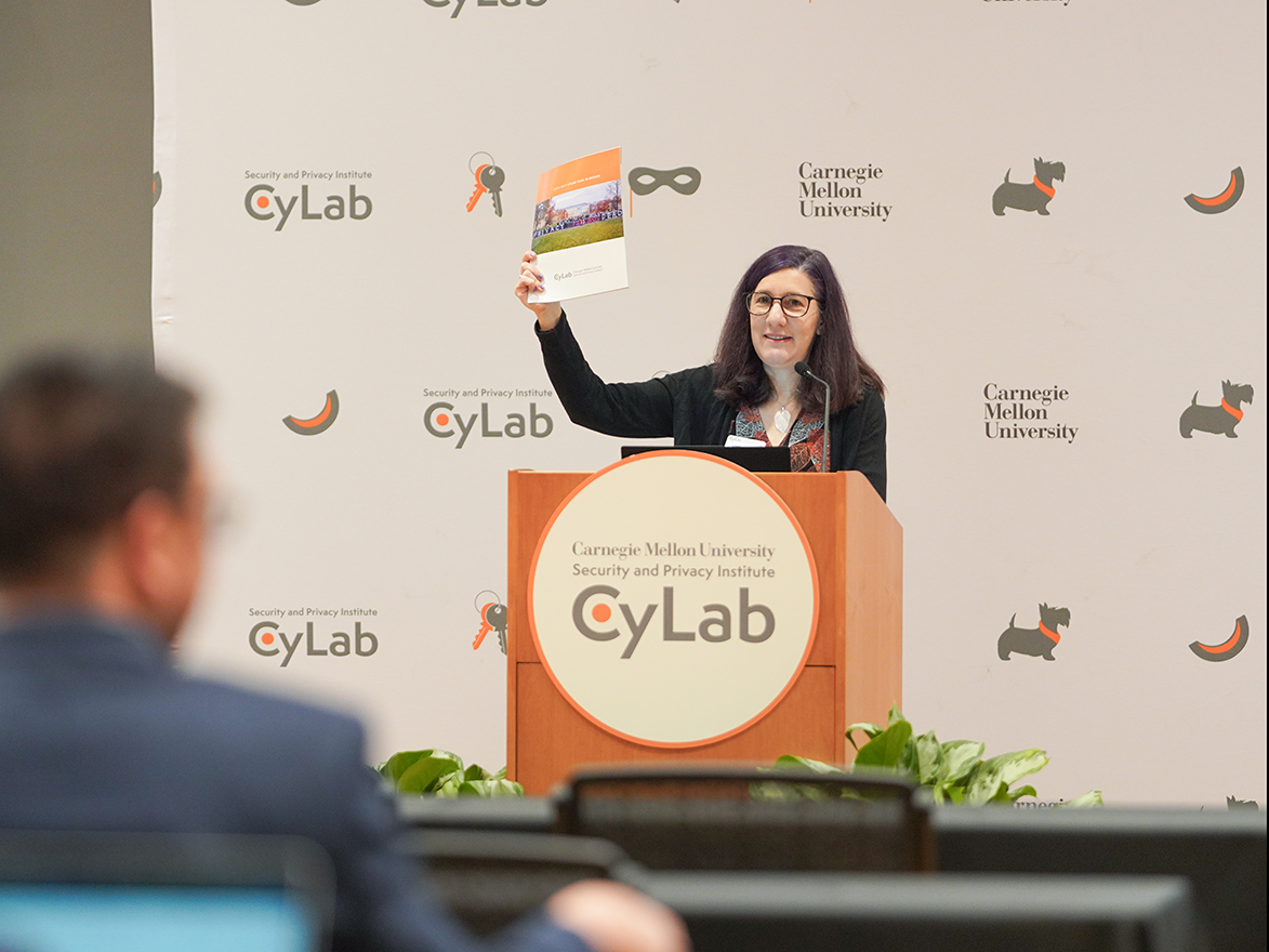 Photo of Lorrie Cranor speaking and holding up a copy of the CyLab Year-in-Review magazine at the 2025 CyLab Partners Conference